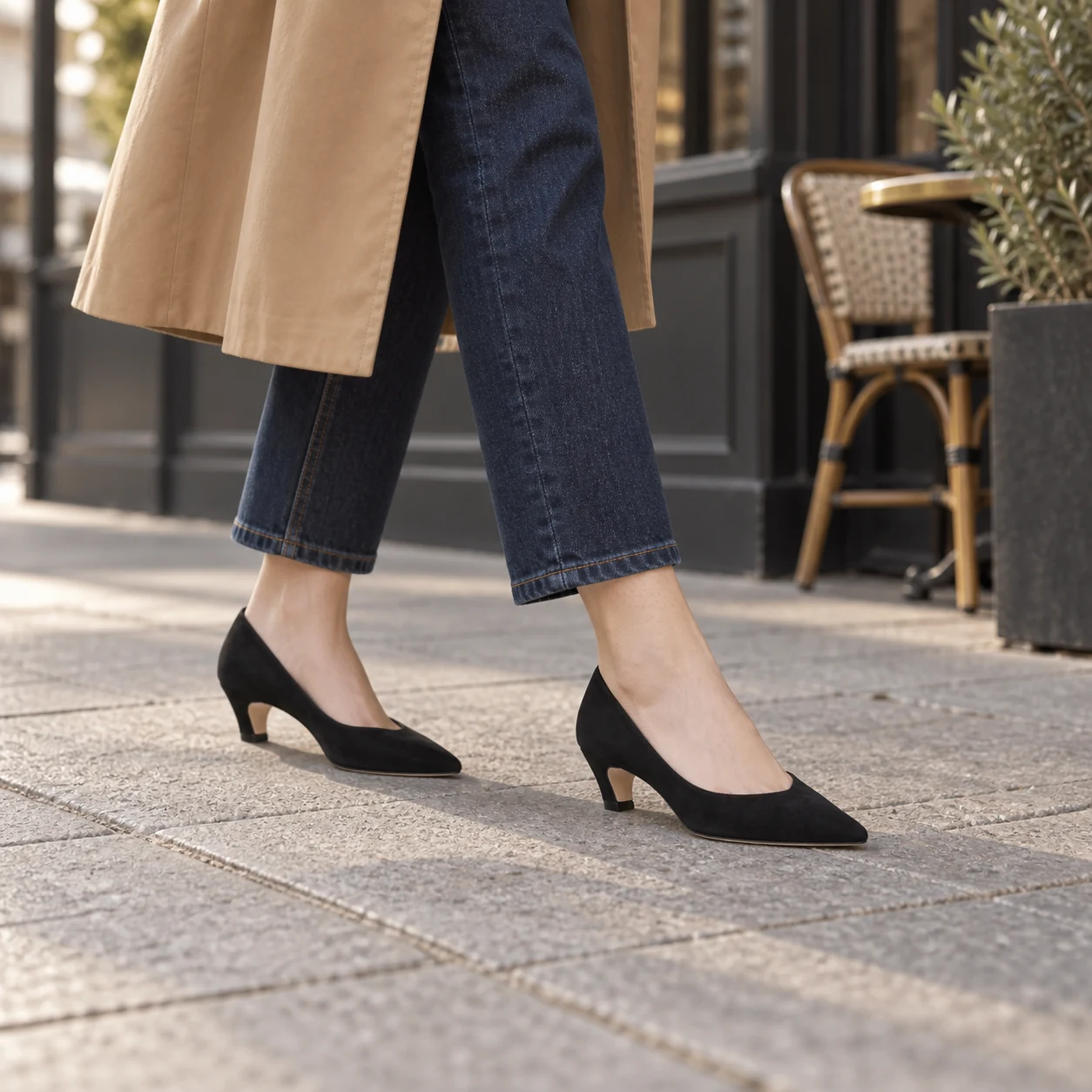 Petite woman wearing black suede kitten heel pumps with cropped jeans and a camel trench coat