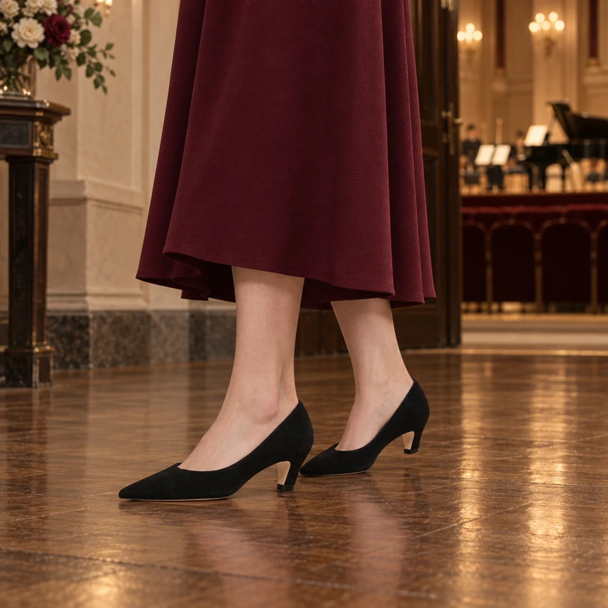 Petite woman wearing black suede kitten heel pumps with a burgundy midi dress at a concert hall