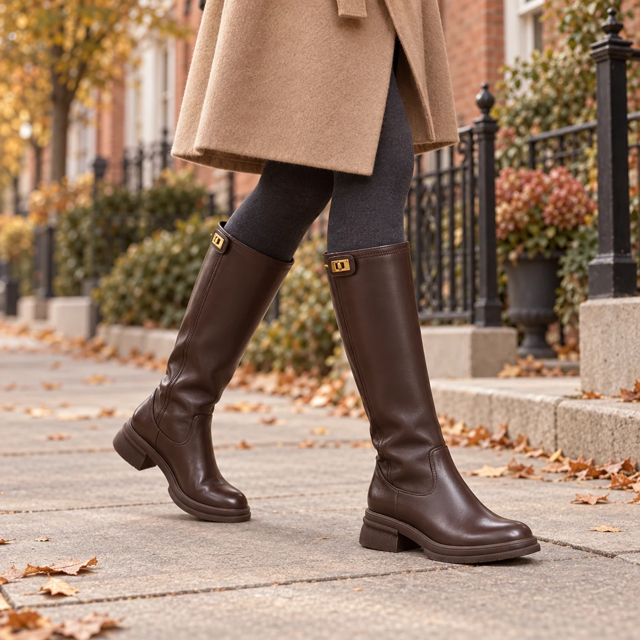 Petite woman walking in brown knee-high boots with a camel coat on an autumn city street
